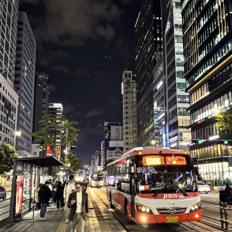 Red city bus at a busy Gangnam Station bus stop at night