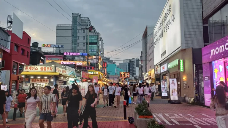 Crowds walking between illuminated shops on Hongdae Red Road in the evening