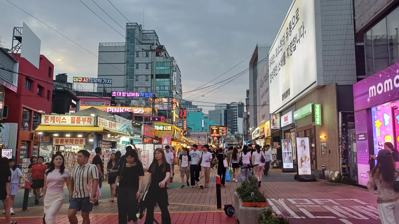 Crowds walking between illuminated shops on Hongdae Red Road in the evening