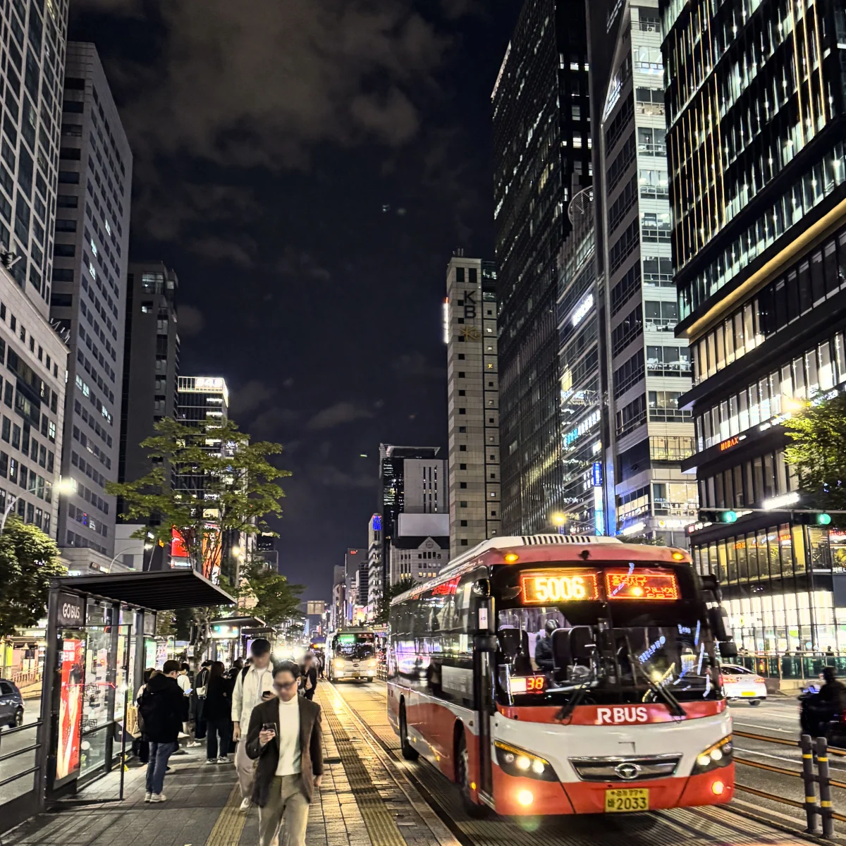 A red bus stopping on a brightly lit boulevard near Gangnam Station at night