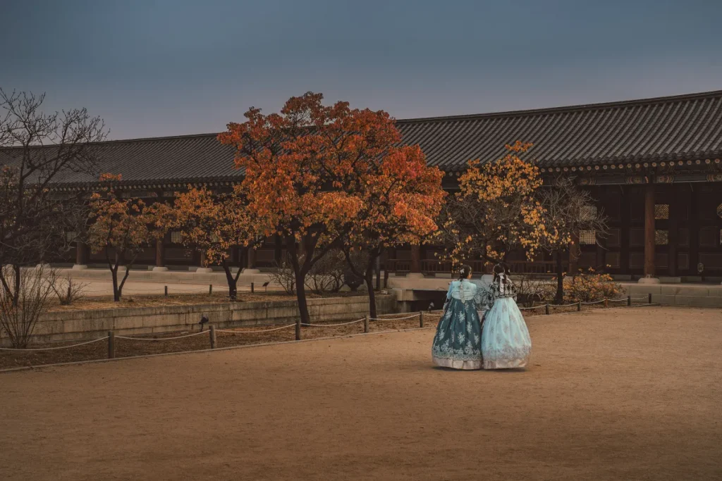 Two visitors wearing blue hanbok walking through Gyeongbokgung Palace in autumn