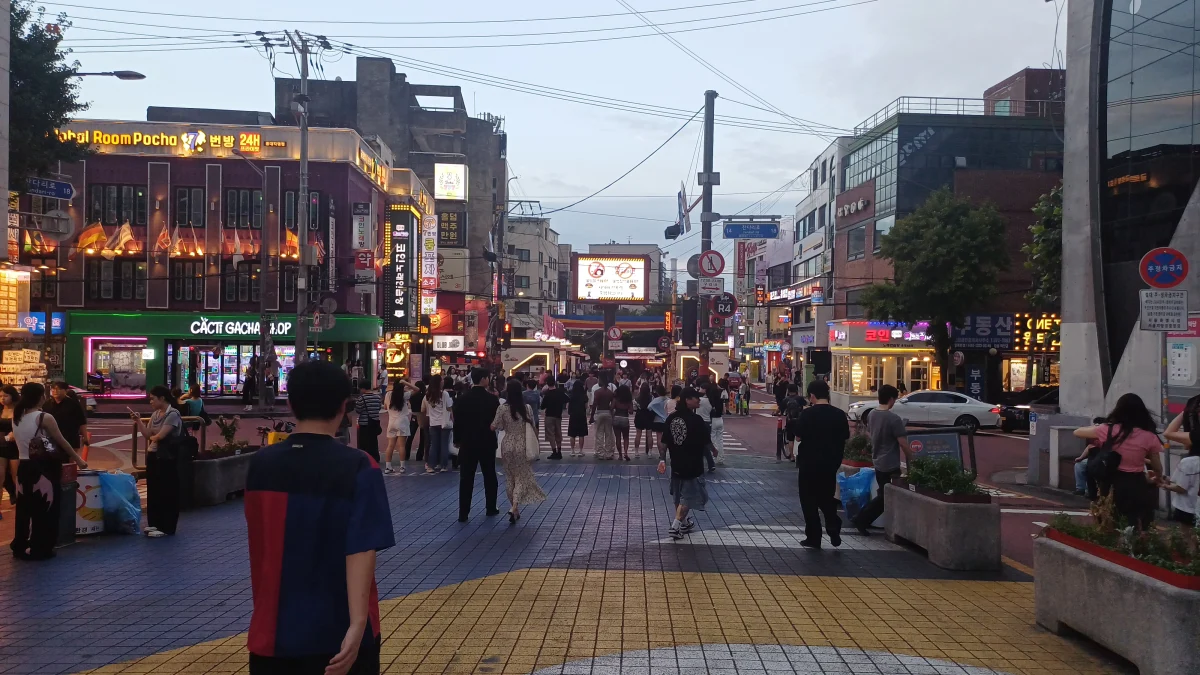 Pedestrians and illuminated storefronts along Hongdae Red Road in the evening
