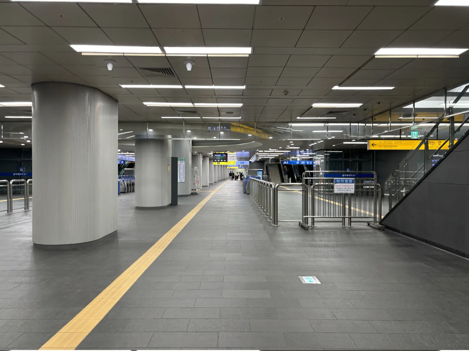 Concourse inside Hongik University Station with signs, escalators, and a tactile guidance path