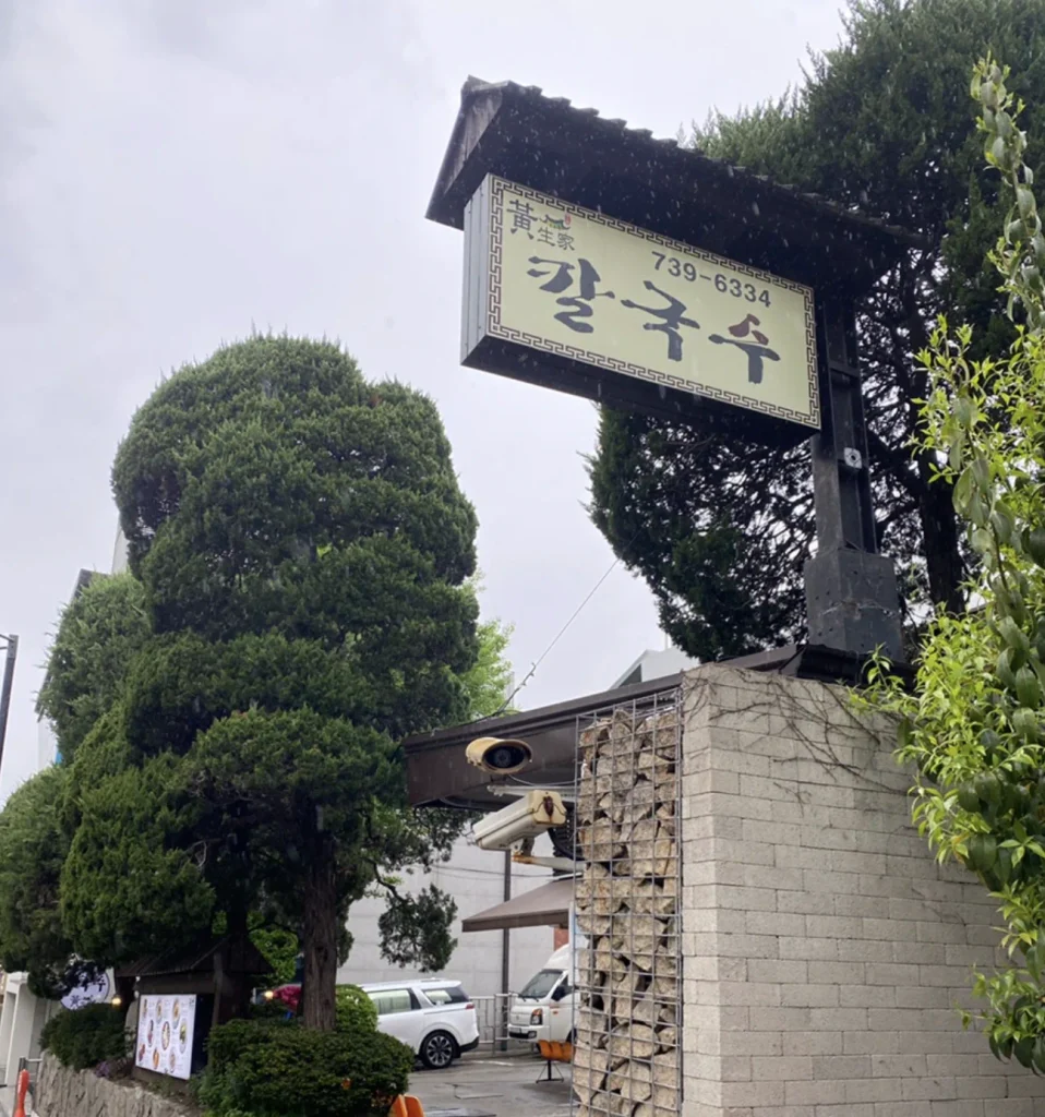 Hwangsaengga Kalguksu entrance sign beside trees on a rainy day