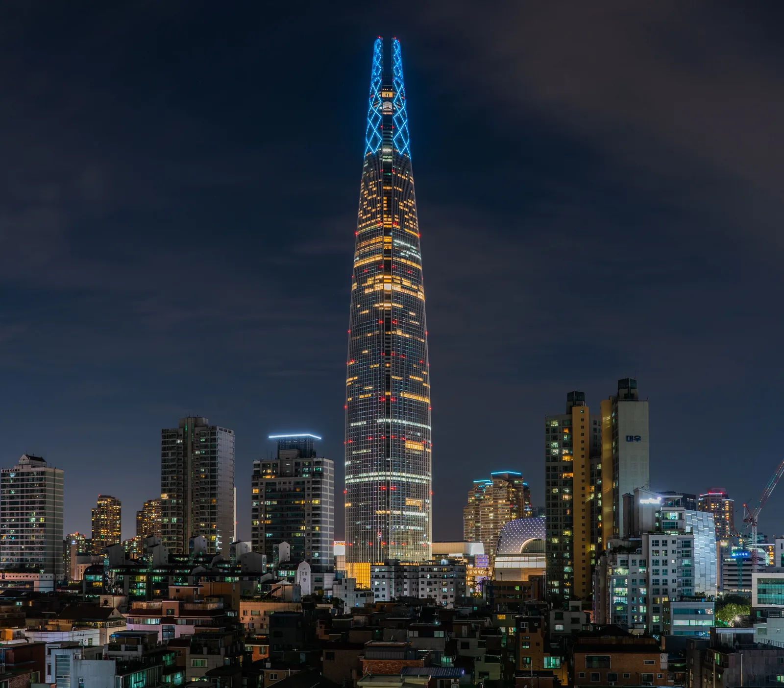 Lotte World Tower illuminated in blue above surrounding Jamsil buildings at night