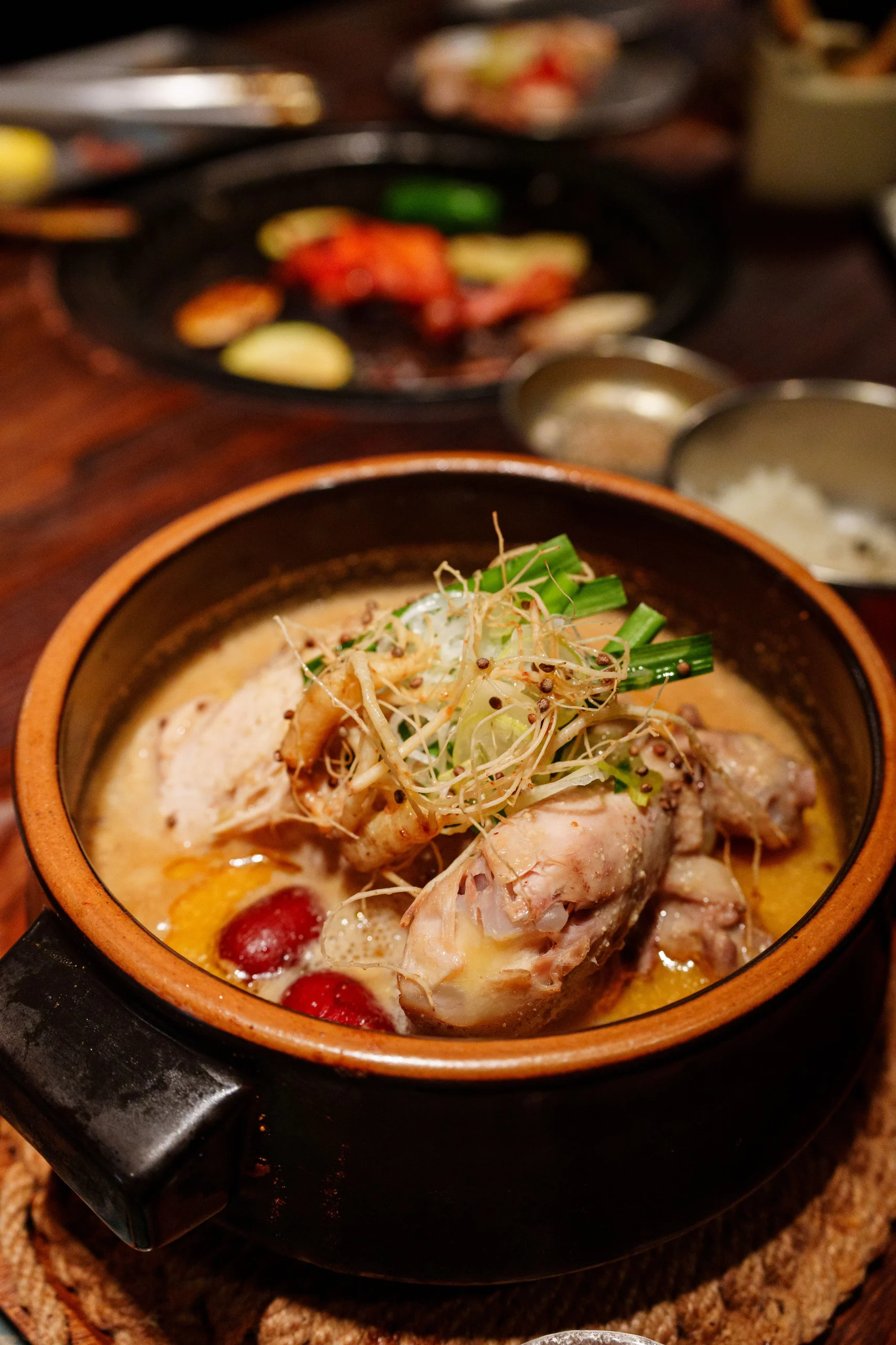 Whole chicken samgyetang in a brown clay pot with jujubes and green garnish