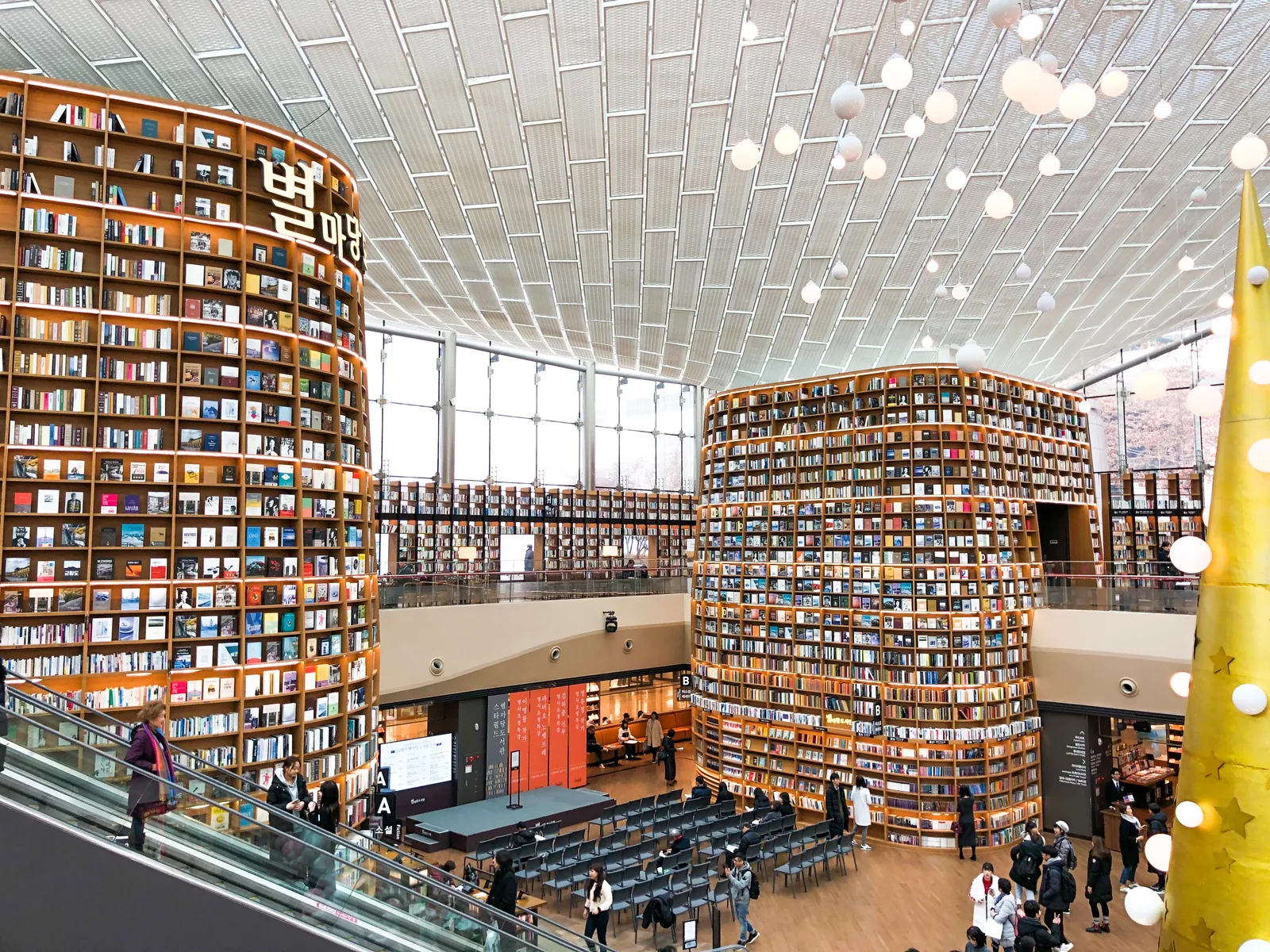 Two tall curved bookshelves, escalators, and the open central floor inside Starfield Library at COEX Mall